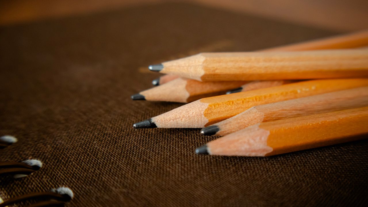A detailed shot of sharpened pencils placed on a brown notebook surface.